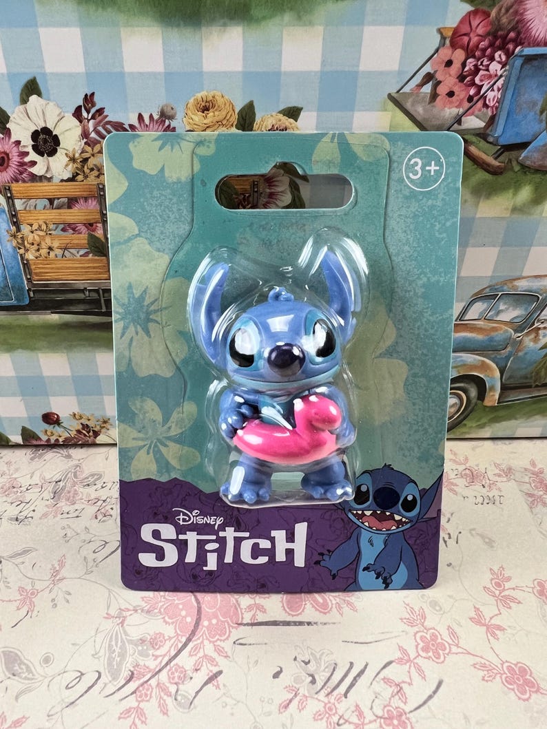 May include: A blue Stitch figurine holding a pink inflatable float, packaged on a teal card with the Disney Stitch logo. The packaging includes a "3+" age recommendation. The background features a floral and vintage car design.