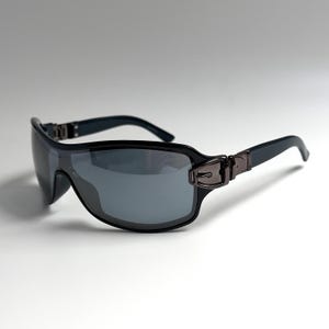 May include: Wraparound sunglasses featuring a single continuous dark gray lens and a black frame. The temples are accented with a metallic buckle-style detail at the hinges, connecting to smooth black arms that curve slightly at the ends.