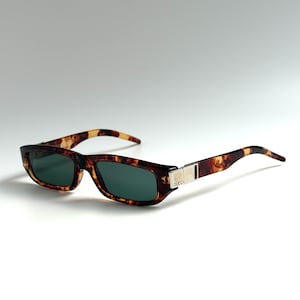 May include: Tortoiseshell sunglasses with green lenses. The rectangular frames have a silver accent on the temples with the brand name "GUCCI". The sunglasses have a classic, retro design.