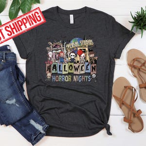 Puede incluir: Una camiseta gris oscuro con un gr&aacute;fico de Universal Studios Halloween Horror Nights con personajes de pel&iacute;culas de terror. El gr&aacute;fico incluye el texto "Universal Studios Halloween Horror Nights".