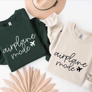 May include: Two sweatshirts, one green and one beige, with the text "airplane mode" and a small airplane graphic printed on the front.