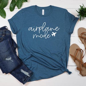 May include: A teal blue t-shirt with the text "airplane mode" in white cursive lettering and a small airplane icon.