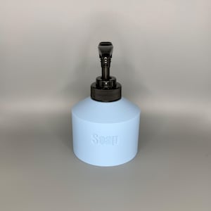 May include: A light blue soap dispenser with a black pump. The word "Soap" is embossed on the front of the dispenser. The dispenser has a cylindrical base and a rounded top.