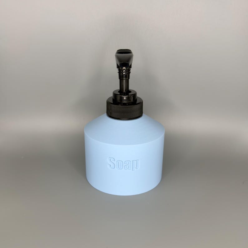 May include: A light blue soap dispenser with a black pump. The word "Soap" is embossed on the front of the dispenser. The dispenser has a cylindrical base and a rounded top.