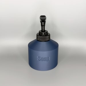 May include: A navy blue soap dispenser with a black pump and a textured surface. The word "Soap" is embossed on the front of the dispenser. The dispenser has a cylindrical base and a black pump head.