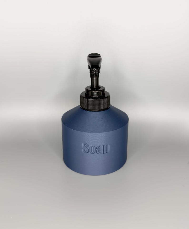 May include: A navy blue soap dispenser with a black pump and a textured surface. The word "Soap" is embossed on the front of the dispenser. The dispenser has a cylindrical base and a black pump head.