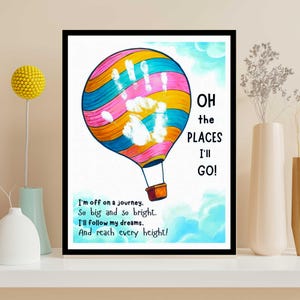 May include: A framed print featuring a colorful hot air balloon with a handprint design. The balloon is striped with pink, blue, yellow, and orange. Text on the print reads "Oh the places I'll go!" and a poem about dreams.