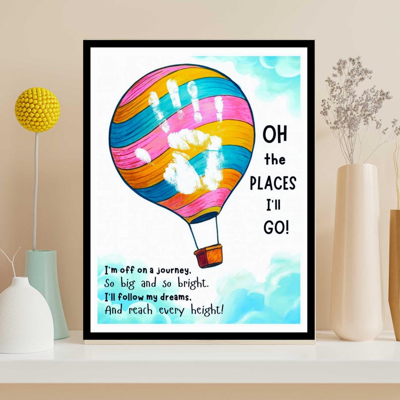 May include: A framed print featuring a colorful hot air balloon with a handprint design. The balloon is striped with pink, blue, yellow, and orange. Text on the print reads "Oh the places I'll go!" and a poem about dreams.