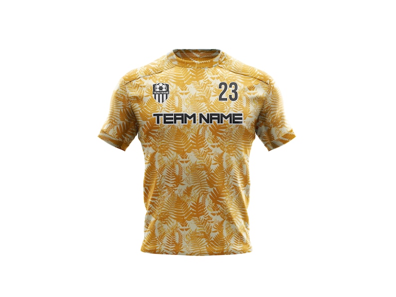 May include: A gold soccer jersey with a fern leaf pattern. The jersey has a black team logo, the number 23, and the text "TEAM NAME".