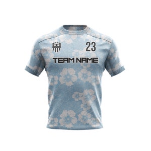 May include: A light blue soccer jersey with a white floral pattern. The jersey has a black team logo, the text "TEAM NAME", and the number "23" printed on the front.