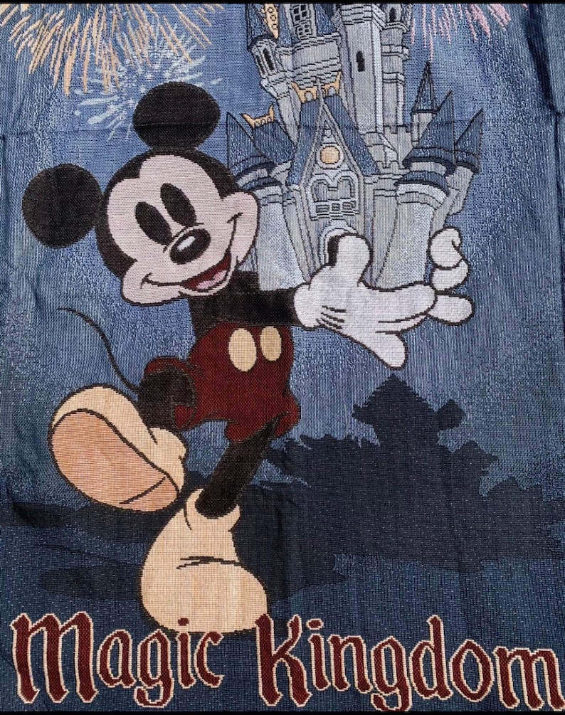 Puede incluir: Un tapiz azul y blanco con Mickey Mouse de pie frente al Castillo de Cenicienta con fuegos artificiales en el fondo. El texto "Magic Kingdom" est&aacute; en la parte inferior del tapiz.