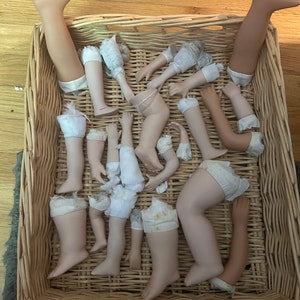 Puede incluir: Una colecci&oacute;n de extremidades de mu&ntilde;ecas, incluyendo piernas y brazos, se encuentra dentro de una cesta de mimbre tejida. Las extremidades son de porcelana o un material similar, con apariencia color carne. Algunas extremidades tienen detalles de tela.