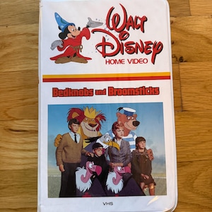 May include: A VHS tape of the Disney film "Bedknobs and Broomsticks." The cover features the film's title in red and yellow, along with a cartoon image of Mickey Mouse as a wizard. The bottom of the cover shows a scene from the movie with the characters.