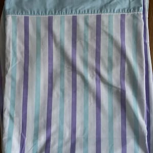 May include: A flat sheet with a light blue top and vertical stripes in white, light blue, and lavender. The sheet is folded, showing the top portion and a section of the striped pattern.