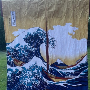 May include: A pair of fabric curtains featuring a Japanese-style print of a large blue wave crashing over a mountain and boats. The curtains are a light yellow color with white and blue accents.
