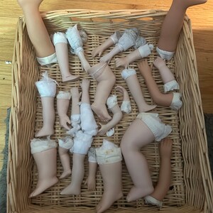 Puede incluir: Una colecci&oacute;n de extremidades de mu&ntilde;ecas de porcelana, incluyendo piernas y brazos, se encuentra dentro de una cesta de mimbre tejida. Las extremidades var&iacute;an en tono de piel y est&aacute;n parcialmente vestidas con tela y encaje.