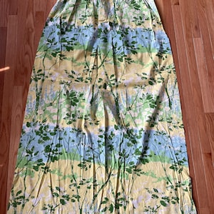 May include: A pair of yellow, green, and blue patterned curtains with a floral design. The curtains have a pleated top and are made of a lightweight fabric.