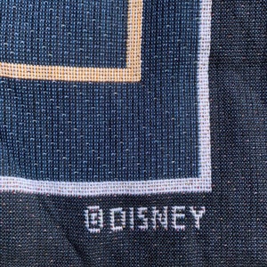 Puede incluir: Primer plano de una tela tejida azul oscuro con un borde blanco y la palabra "DISNEY" bordada en blanco.