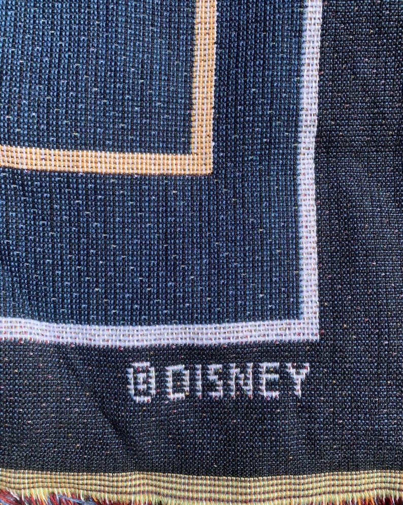Puede incluir: Primer plano de una tela tejida azul oscuro con un borde blanco y la palabra "DISNEY" bordada en blanco.