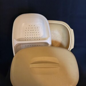 Puede incluir: Un juego de vaporera de plástico beige que consta de un recipiente base rectangular, una bandeja insertable perforada extraíble con un divisor central y una tapa rectangular a juego con un asa elevada en la superficie superior.