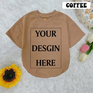 May include: A brown short-sleeved t-shirt with a white box that says "YOUR DESIGN HERE" on the front.