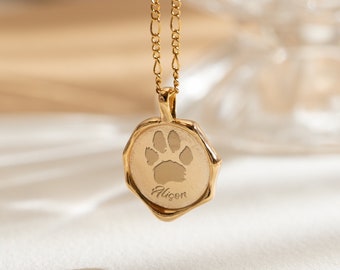Puede incluir: Collar de oro con un colgante redondo que presenta una huella de pata y el nombre "Aicon" grabado en él.