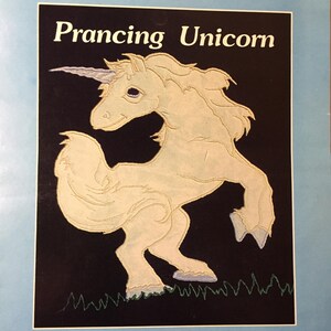May include: A cream-colored prancing unicorn illustration with a purple horn and flowing mane, set against a black background. The text "Prancing Unicorn" is displayed at the top. Green grass is at the bottom.