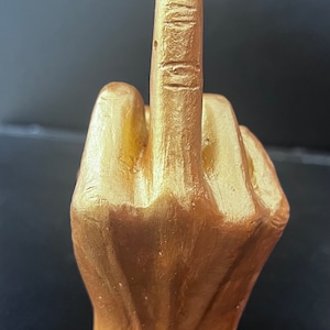 May include: A gold-coloured hand sculpture making the middle finger gesture.