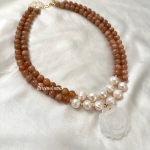 May include: A double-strand necklace with brown sunstone beads and white pearls. The necklace has a white jade rose pendant.
