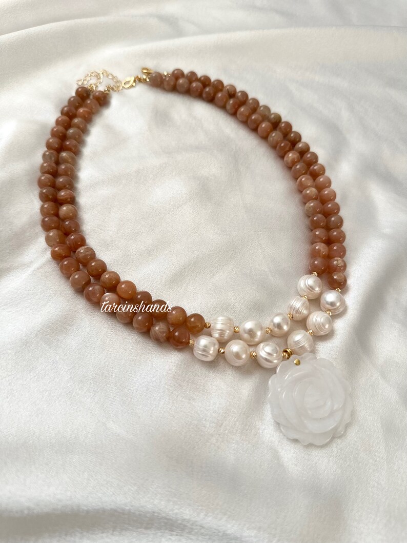 May include: A double-strand necklace with brown sunstone beads and white pearls. The necklace has a white jade rose pendant.