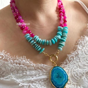May include: A layered necklace with pink and turquoise beads and a large turquoise agate pendant. The necklace is on a white lace background.