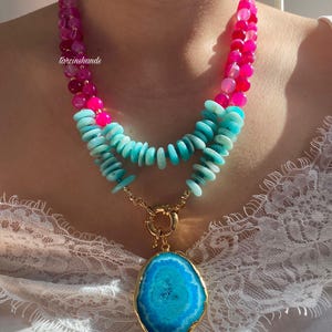 May include: A layered necklace with a large blue agate pendant. The necklace features pink and turquoise beads.