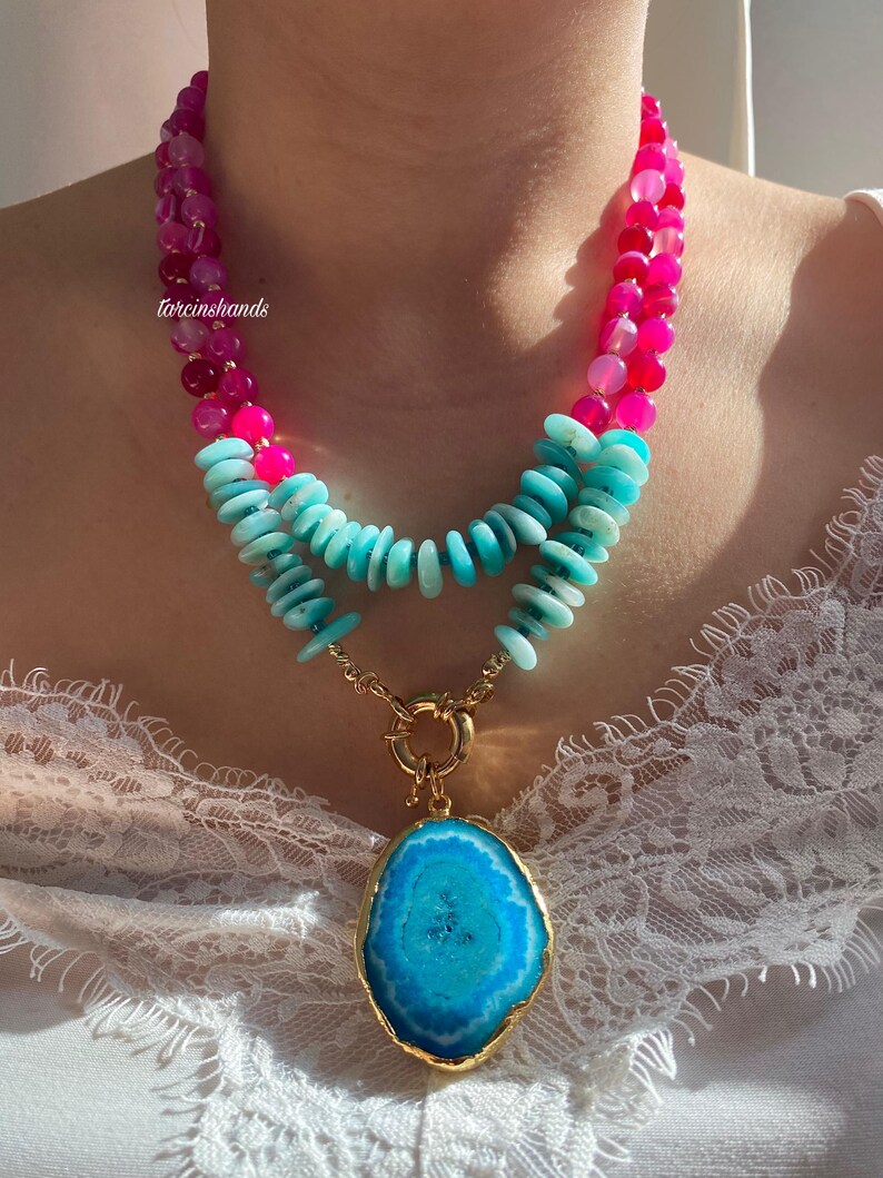 May include: A layered necklace with a large blue agate pendant. The necklace features pink and turquoise beads.