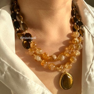 May include: A double-strand necklace with a teardrop pendant. The necklace is made of tiger's eye and citrine beads. The pendant is also made of tiger's eye.