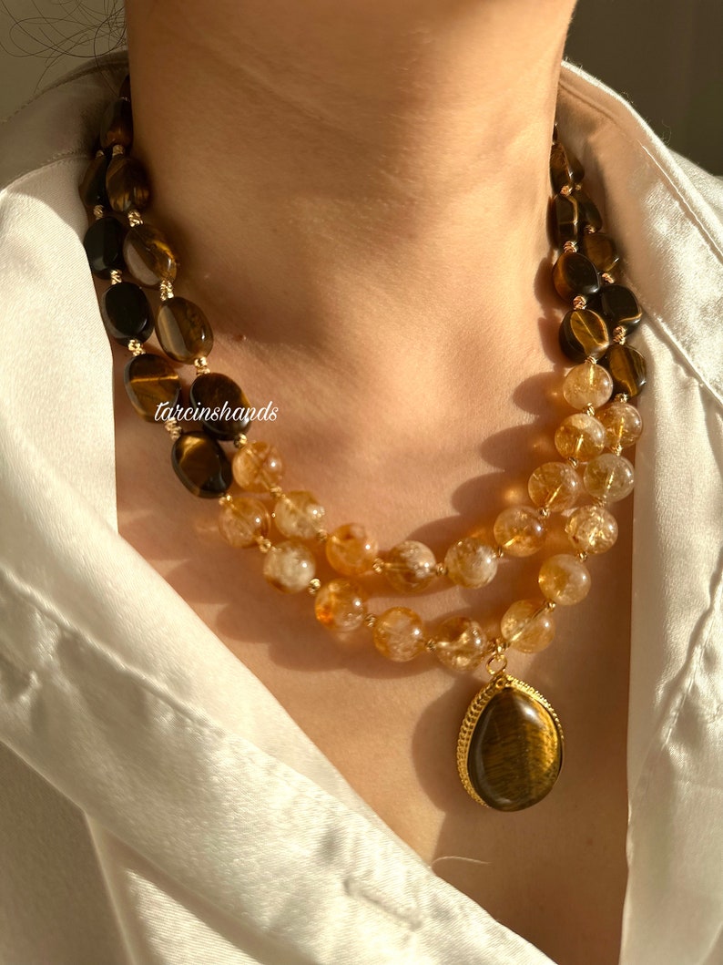 May include: A double-strand necklace with a teardrop pendant. The necklace is made of tiger's eye and citrine beads. The pendant is also made of tiger's eye.