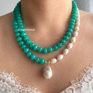 Puede incluir: Collar de dos hilos con cuentas turquesas y perlas blancas. Un gran colgante de perla barroca cuelga del collar. Se ven detalles dorados. El texto "tarcinshands" est&aacute; en el lado izquierdo de la imagen.