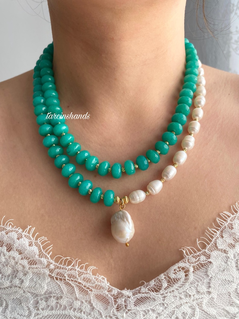 Puede incluir: Collar de dos hilos con cuentas turquesas y perlas blancas. Un gran colgante de perla barroca cuelga del collar. Se ven detalles dorados. El texto "tarcinshands" est&aacute; en el lado izquierdo de la imagen.