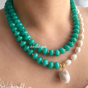 Puede incluir: Un collar de varias capas con cuentas de color turquesa y perlas blancas. El collar tiene detalles dorados y un colgante de perla grande de forma irregular. El texto "tarcinshands" es visible en el collar.