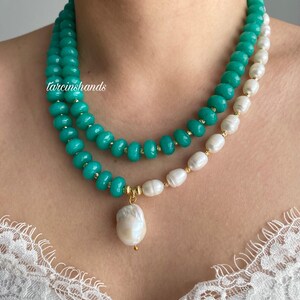 Puede incluir: Un collar de dos hilos con cuentas turquesas y perlas blancas. Las cuentas turquesas est&aacute;n ensartadas con detalles dorados. Un gran colgante de perla barroca blanca cuelga del collar. El texto "tarcinshands" es visible.