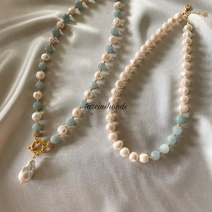 May include: Two pearl necklaces with gold clasps and accents. One necklace features a teardrop pearl pendant and alternating light blue beads. The other necklace has alternating light blue beads.