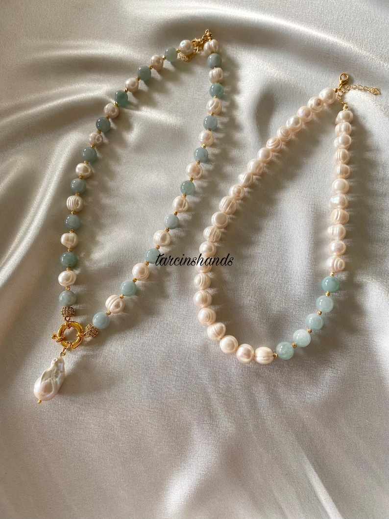 May include: Two pearl necklaces with gold clasps and accents. One necklace features a teardrop pearl pendant and alternating light blue beads. The other necklace has alternating light blue beads.