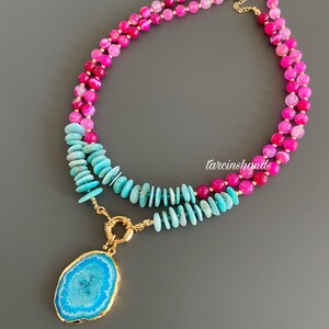 May include: A layered necklace with a large blue agate pendant. The top layer is made of pink and white agate beads, and the bottom layer is made of turquoise beads.