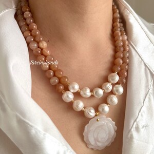 May include: A double-strand necklace with a rose-shaped pendant. The top strand is made of peach-colored sunstone beads, and the bottom strand is made of white pearls. The pendant is made of white jade and has a carved rose design.