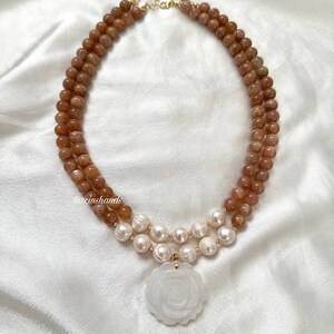 May include: A double-strand necklace with brown sunstone beads and white pearls. The necklace has a large white carved rose pendant.