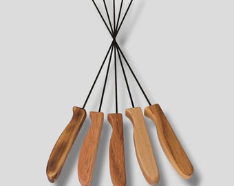 May include: A set of five fondue forks with long, thin black metal shafts and contoured wooden handles. Each handle features a unique wood grain pattern in varying shades of brown, ranging from light tan to a darker, toasted brown finish.