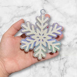 May include: A white snowflake ornament with iridescent glitter, featuring a loop for hanging.