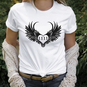 May include: White t-shirt featuring a black graphic of angel wings forming a heart with the number 1111 inside.