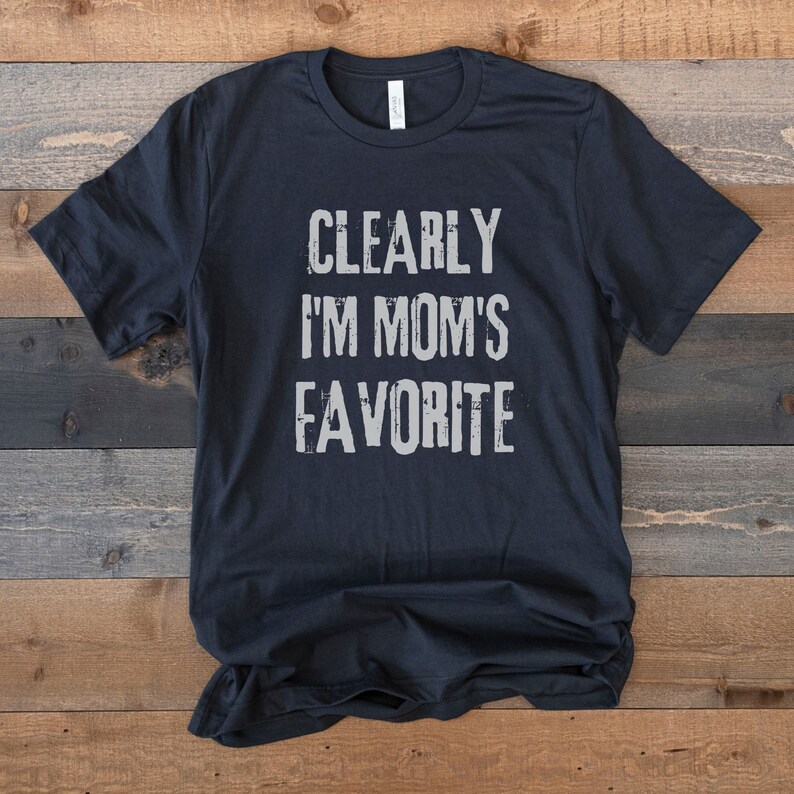 May include: Black t-shirt with the text "CLEARLY I'M MOM'S FAVORITE" in white.