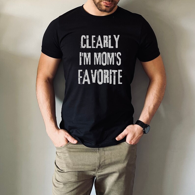 May include: A black t-shirt with the text "CLEARLY I'M MOM'S FAVORITE" in white lettering.