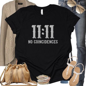 May include: Black t-shirt with the text "11:11 NO COINCIDENCES" in a grey font. The shirt is being modelled with a cardigan, jeans and sandals.